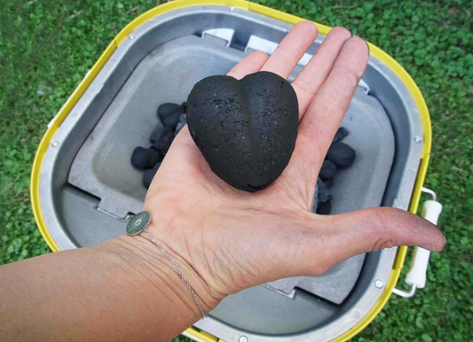 Une personne tient dans sa main du charbon en forme de coeur au dessus d'un barbecue 