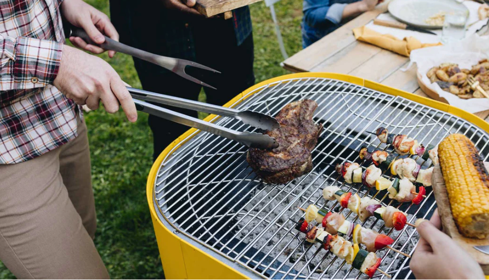 Une personne cuisine de la viande et des légumes sur un barbecue jaune